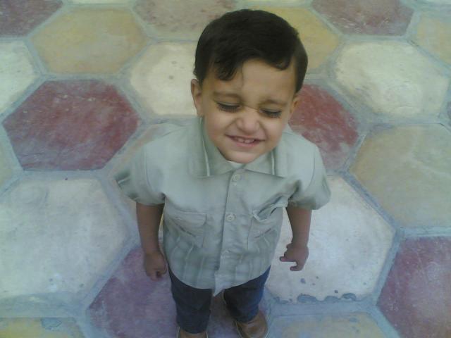 A toddler standing on hexagonal floor tiles, grinning with eyes shut