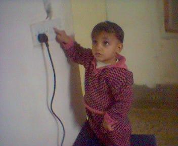 A small child reaching up to a wall socket, pulling at the cable plugged into it
